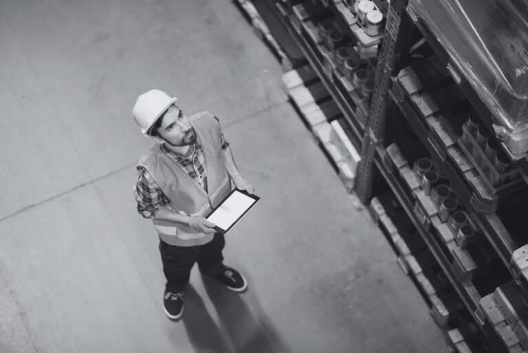 Warehouse worker employed by staffing service checking inventory on tablet.